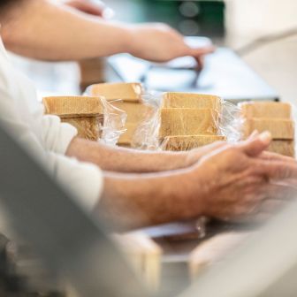 Das Bild zeigt eine Mitarbeiterin in der ChäsChuchi an der Schneidemaschine beim Käse schneiden. Baumann Käse verarbeitet und konfektioniert die Käse weiter.